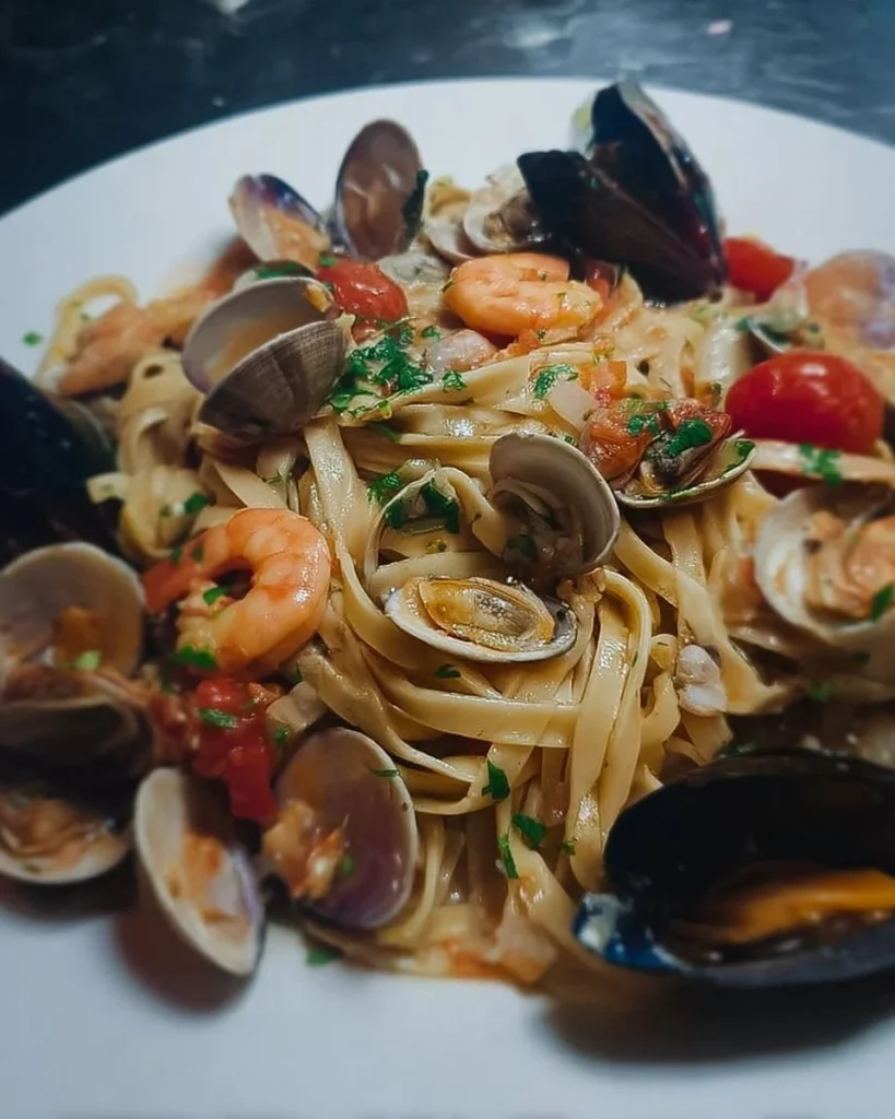 Fettucce mit Kirschtomaten, Garnelen, Muscheln und Venusmuscheln auf einem Teller